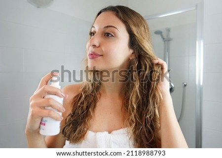 Hair thermal protection. Smiling woman with healthy beautiful long wavy hair applying thermal protect hair spray. Haircare Cosmetic. Royalty-Free Stock Photo #2118988793