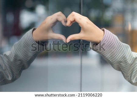 The woman put one of her hands against the mirror to symbolize a heart that represents friendship, kindness and love. The concept of friendship, love, kindness between friends, family and lovers.