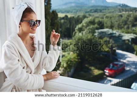 Attractive young woman in a white robe on the balcony bit on green nature unaltered