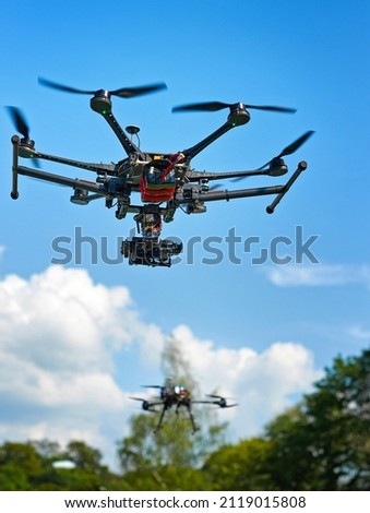 Two drones with camera flying in the blue sky above the trees. Shooting photos and video from the air. Quadcopters in the forest.