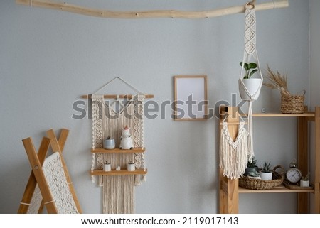 Stylish and modern boho-style nursery interior with mock-up photo frame, macrame hanging wall shelves, children's tent, wooden shelving and elegant accessories. Designer home decor. Mockup. Royalty-Free Stock Photo #2119017143