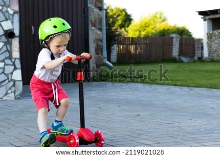 Toddler in a helmet rides a red scooter in the yard.