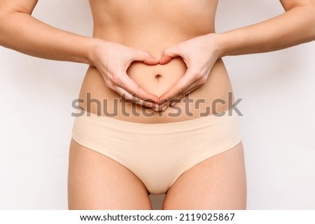 Cropped shot of a young slender woman forming heart shape with her hands on stomach isolated on a white background. Health care, good digestion