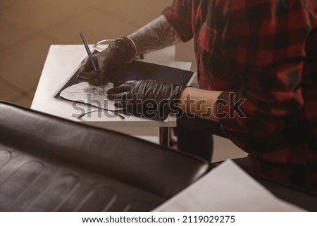 Photo of female hands of tattoo master in black gloves drawing picture for client