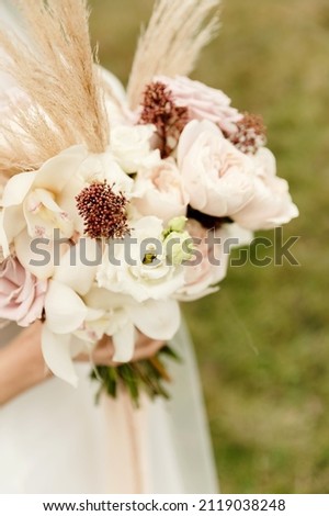 a beautiful bride in a white dress and with a wedding bouquet of dried flowers is in the autumn mountains among the yellow grass