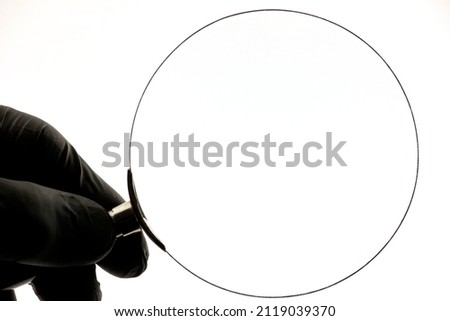 A hand in a black glove holds a magnifying glass isolated on a white background