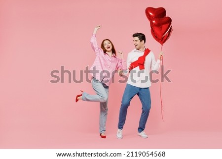 Full size young couple two friend woman man in shirt hold bunch of red inflatable balloons dance isolated on plain pastel pink background studio portrait Valentine's Day birthday holiday party concept