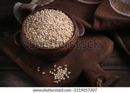 Bowl of dry raw broken pearl barley cereal grain on dark wooden background. Cooking pearl barley porridge concept. Royalty-Free Stock Photo #2119057307
