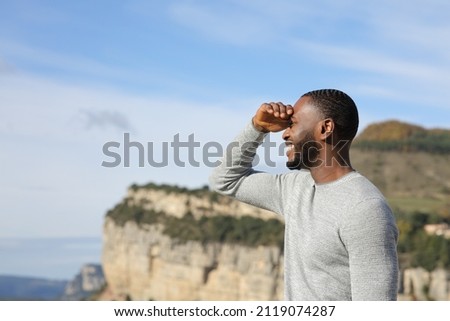 Happy man with black skin searching looking away protecting from sun with his hand in the mountain Royalty-Free Stock Photo #2119074287