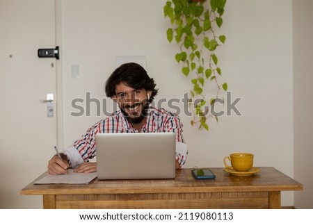 Young business man working at home with laptop on a brown arm chair. Gray notebook for working. Home office concept. High quality photo