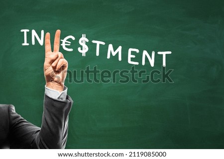 Trade market, victory and investing concept with man fingers showing V letter in Investment word handwritten on green empty blackboard on backdrop. Mockup