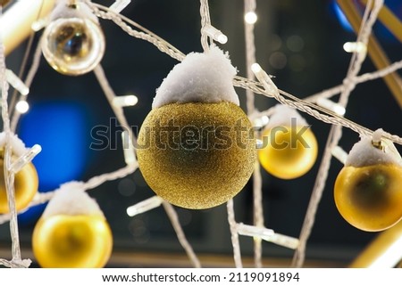Gold balls and garlands hanging under snow. Christmas installation