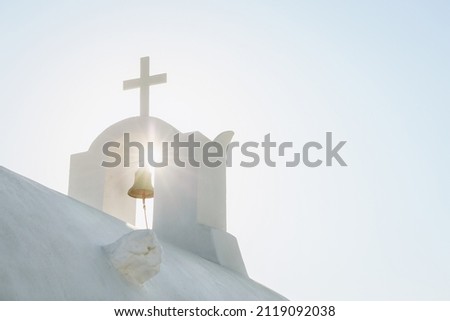 White Orthodox Church belfry with cross and bell in sunshine on sky background. Santorini island, Greece Royalty-Free Stock Photo #2119092038