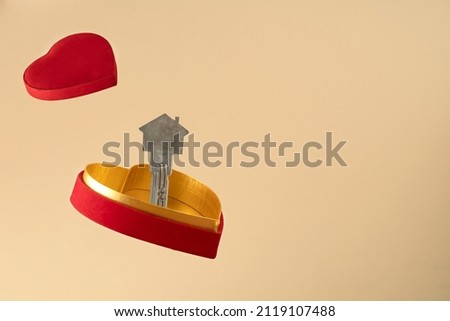 Close up photo of floating  heart shaped gift box and house shaped door key. concept of real estate , buying house on valentines day as a gift.
