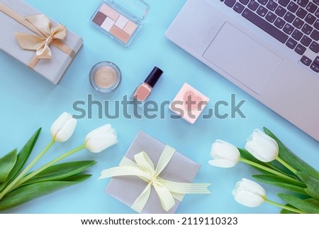 Laptop, gift boxes, makeup cosmetics and tulip flowers on blue background. Spring holidays, online shopping concept. Top view, flat lay.