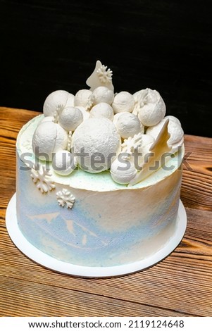 White blue sponge coconut delicious vanilla creamy frosting cake decorated with big round marshmallow, chocolate snowflakes, fir trees,mountain picture, sweet dessert on wooden black table top view