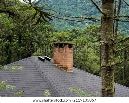 brick chimney in a grey roof. Green landscape as background