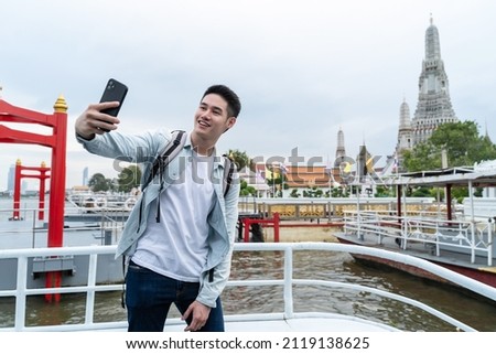Asian young male backpacker use smartphone selfie take picture in city. Handsome man tourist traveler wear mask travel alone on street, use smartphone record vlog on holiday vacation trip in Thailand