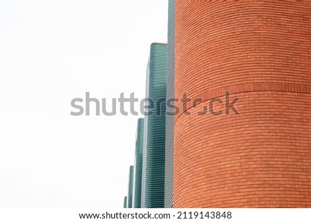 Green metal exterior wall panels with small symmetric line patterns running horizontally on multiple panels. The tall red brick wall is curved and circular in design. The background is white.