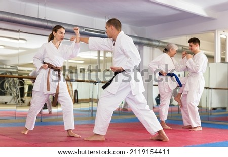 Determined young girl wearing kimono practicing martial arts techniques paired with experienced trainer in training room
