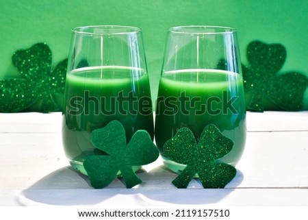 Happy St. Patrick's Day. Two glass green beer with clover leaves on white table on green background. Selective focus. Happy Patricks day postcard