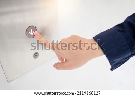 Male forefinger pressing on down symbol button of elevator or lift.