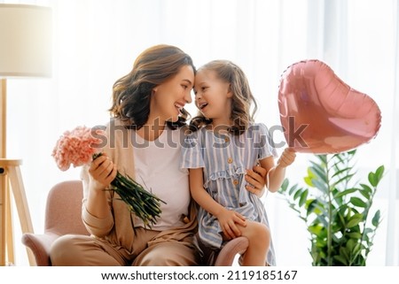 Happy day! Child daughter is congratulating mother and giving her flowers. Mum and girl smiling and hugging. Family holiday and togetherness.