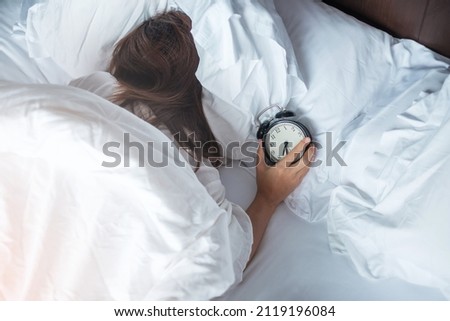 alarm clock and asian woman hand stop time in bed while sleeping, young adult female wake up late in the morning. Relaxing , sleepy, daily routine and have a nice day concepts Royalty-Free Stock Photo #2119196084