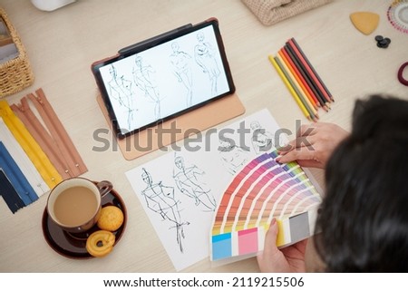 Fashion designer having cup of coffee when choosing color palette for new collection, view from above