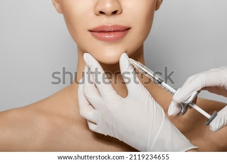Syringe near woman's chin, beauty injections with fillers for chin shape correction. Cropped female face while procedure chin contouring Royalty-Free Stock Photo #2119234655