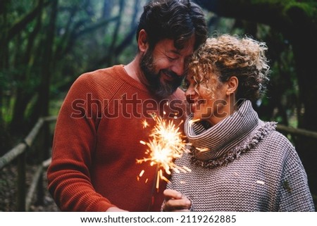 Romantic adult couple enjoy and love together with fire sparkler light in the forest green trees background. Man and woman with tenderness and relationship celebrate with firelight and smile Royalty-Free Stock Photo #2119262885