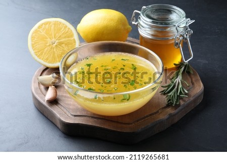 Bowl with lemon sauce and ingredients on dark table. Delicious salad dressing Royalty-Free Stock Photo #2119265681