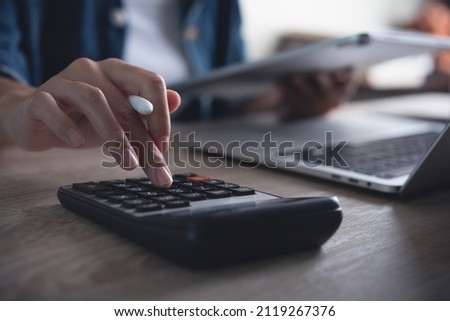 Business woman using calculator to calculate financial report, working at office with laptop computer on table. Asian female accountant or banker making calculations. finances and economy concept Royalty-Free Stock Photo #2119267376