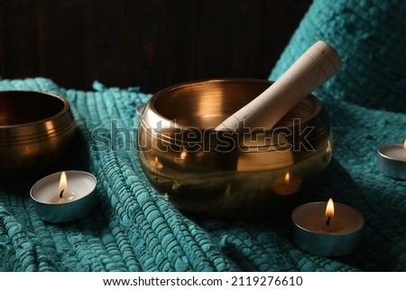 Tibetan singing bowls with mallet and burning candles on turquoise fabric