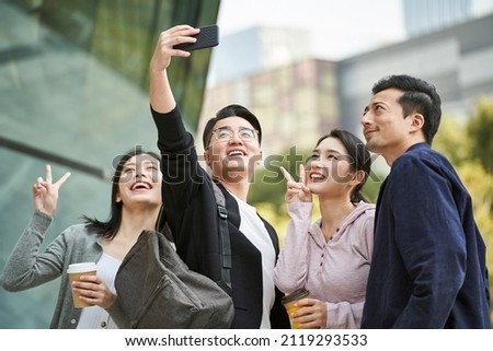 group of young asian people taking a selfie using cellphone outdoors on street happy and smiling