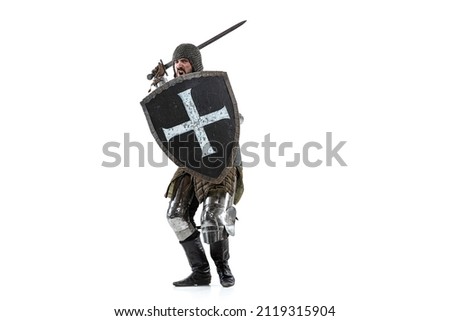Portrait of brutal serious man, medieval warrior or knight in protective covering with sword preparing to attack isolated over white studio background. Comparison of eras, history, renaissance style Royalty-Free Stock Photo #2119315904