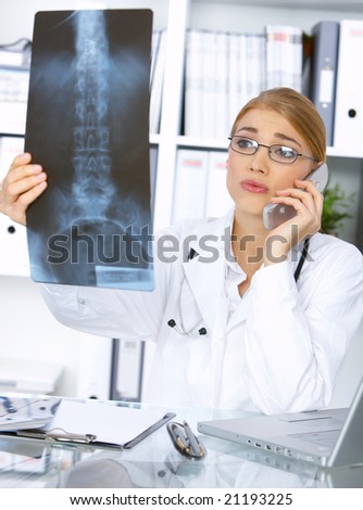 Portrait of female doctor examining x-ray picture and talking cell