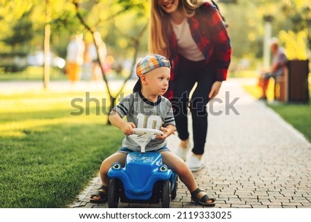 Happy cute boy ride a child's car, walking in the park with mom, mom teaches her son to ride a car in the park on a summer day