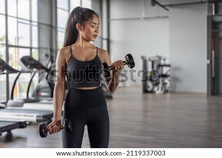 Asian woman exercise in fitness. Young healthy woman in sportswear doing arms exercise in fitness. Royalty-Free Stock Photo #2119337003
