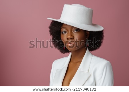 Elegant beautiful Black woman wearing classic white blazer, stylish fedora hat, posing in studio, on pink background. Close up portrait. Copy, empty space for text
 Royalty-Free Stock Photo #2119340192
