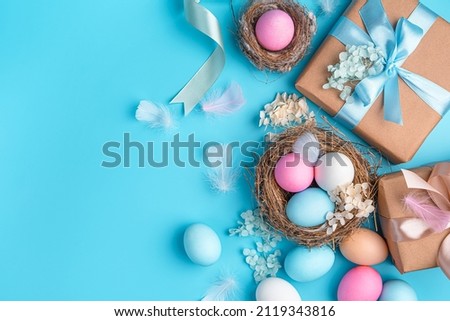 Easter background with colored eggs, nests and gifts on a blue background. Happy Easter. Top view, copy space. Royalty-Free Stock Photo #2119343816