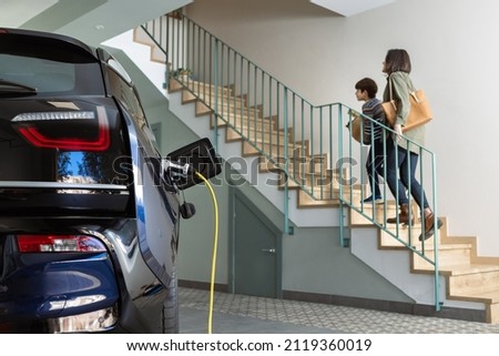 Plugged cable charging an electric family car in a particular garage. Royalty-Free Stock Photo #2119360019