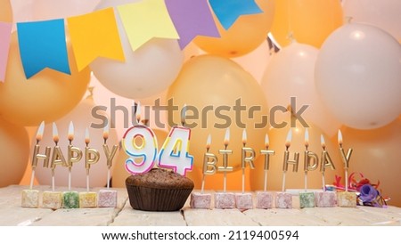 Happy birthday greetings for 94 years old from gold letters of candles burning against the background of mine space balloons. Beautiful birthday card with a muffin for ninety-four years.