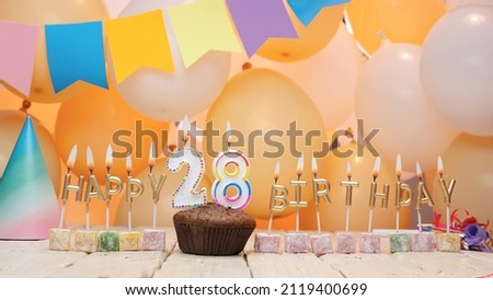 Happy birthday greetings for 28 years old from golden letters of candles burning against the background of mine space balloons. Beautiful birthday card with a muffin for twenty-eight years