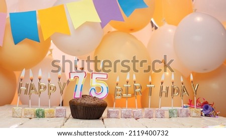Happy birthday greetings for 75 years from gold letters of candles burning against the background of mine space balloons. Beautiful birthday card with a muffin for seventy-five years