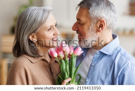 Loving mature husband giving happy wife bouquet of tulips at home, senior man congratulating beloved woman with flowers on March 8. Lovely elderly couple celebrate anniversary. Selective focus Royalty-Free Stock Photo #2119413350