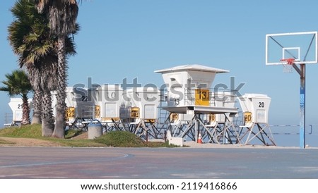 Palm trees and basketball sport field or court on beach, California coast, USA. Streetball playground on shore and lifeguard stand, tower ot station. Mission beach, San Diego. Hoop, backboard and sky.