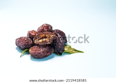 Dried dates and green leaves on a light blue background close-up.