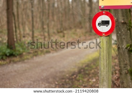 No cars and trucks allowed stop sign on a wooden post in the forest near rural road, no people.
