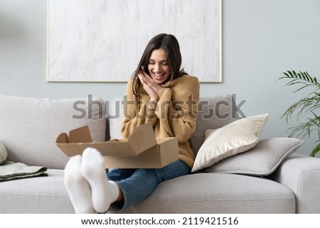 Happy young woman sit on couch in living room unpack cardboard box buying goods on Internet, smiling excited millennial girl open carton parcel order, shopping online, good delivery concept Royalty-Free Stock Photo #2119421516
